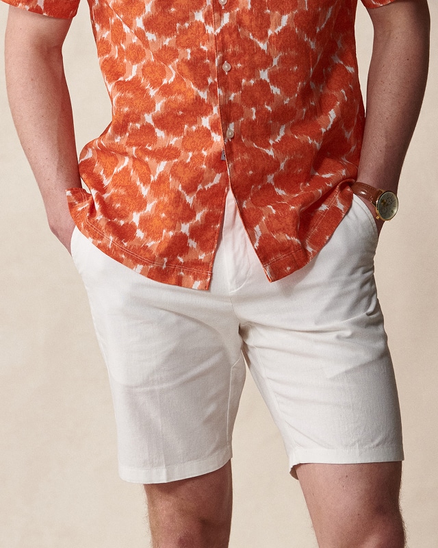 Man in an orange patterned shirt and white shorts. Pants and shorts up to 30 percent off.