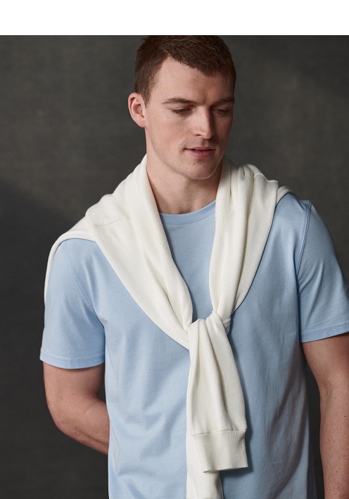 Man in a light blue t-shirt with a cream sweater over his shoulders. Casual shirts 30 percent off.