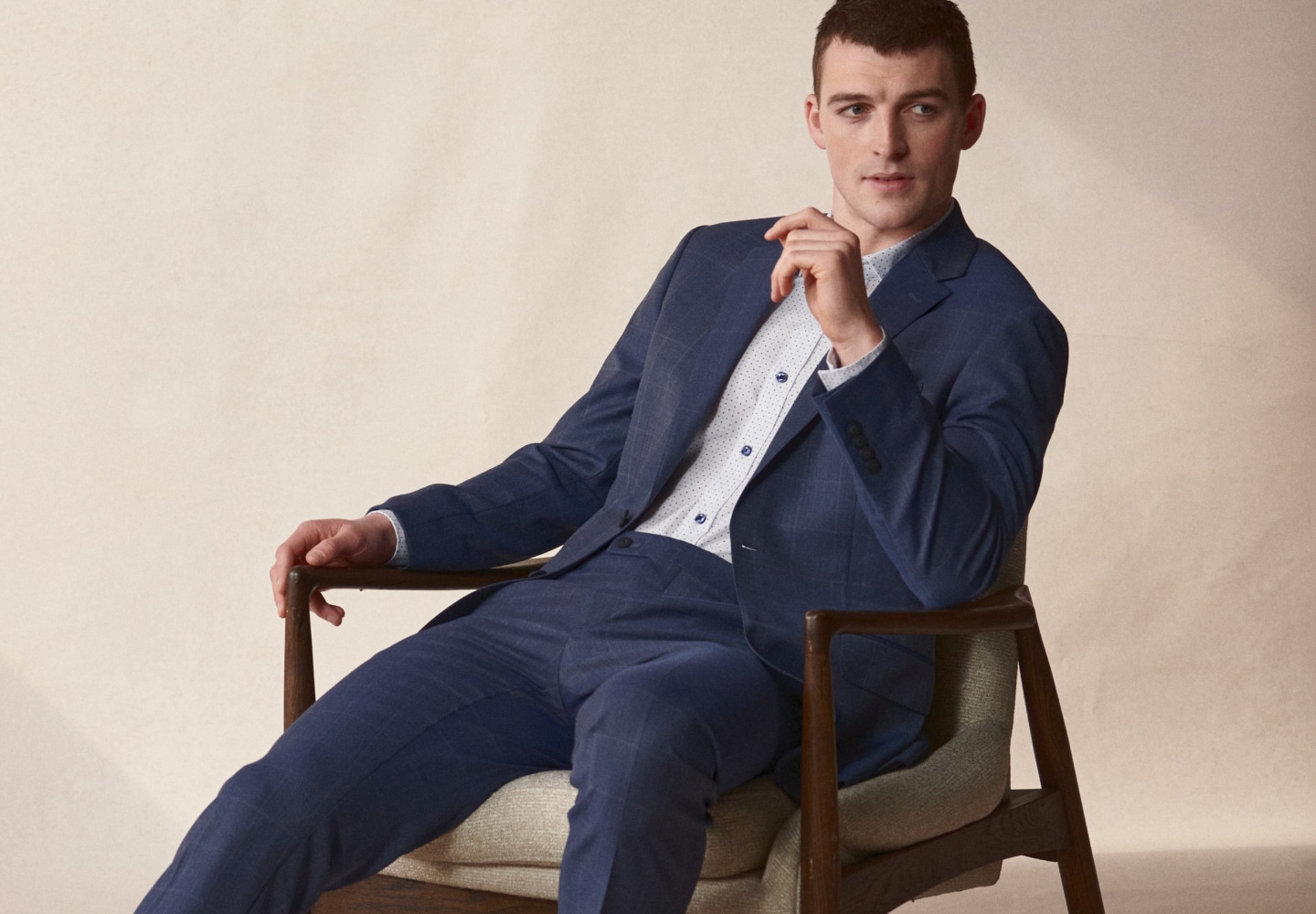 Man in a blue windowpane suit seated in a chair. Online only suits 30 percent off.