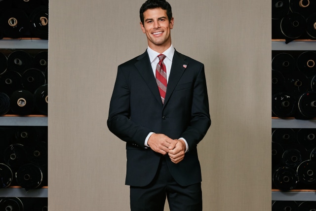Man wearing a navy suit with an American flag lapel pin in a tailoring studio.