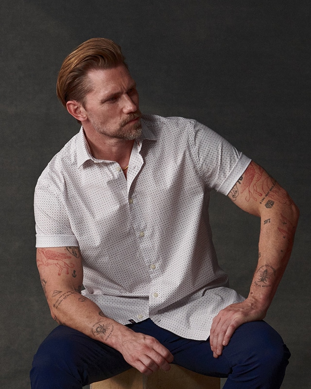Man sitting wearing a white printed short-sleeve shirt. Casual wear buy 1 get 1 50 percent off.