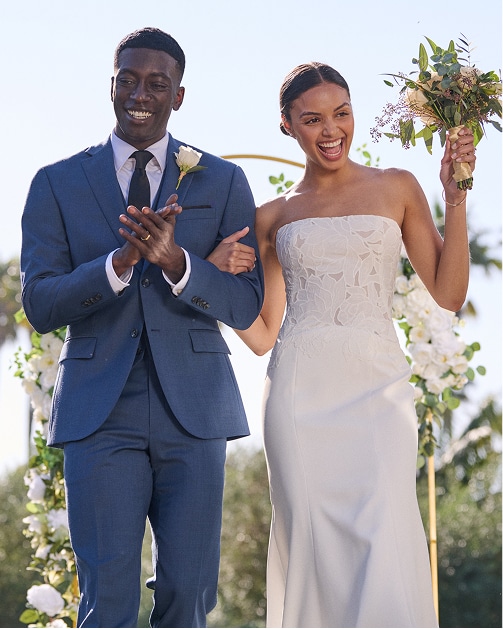 Couple under a floral wedding arch. Groom in a blue suit