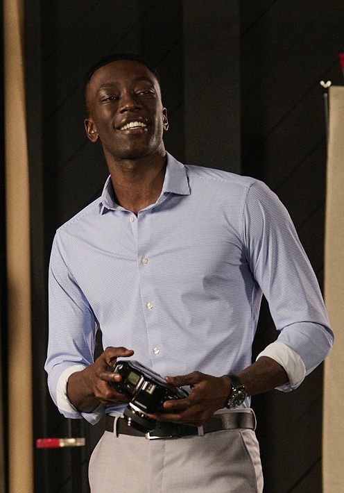 Man in a light blue striped dress shirt holding a camera.