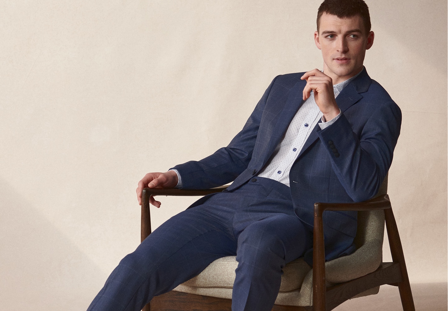 Man wearing a navy windowpane suit seated in a chair.