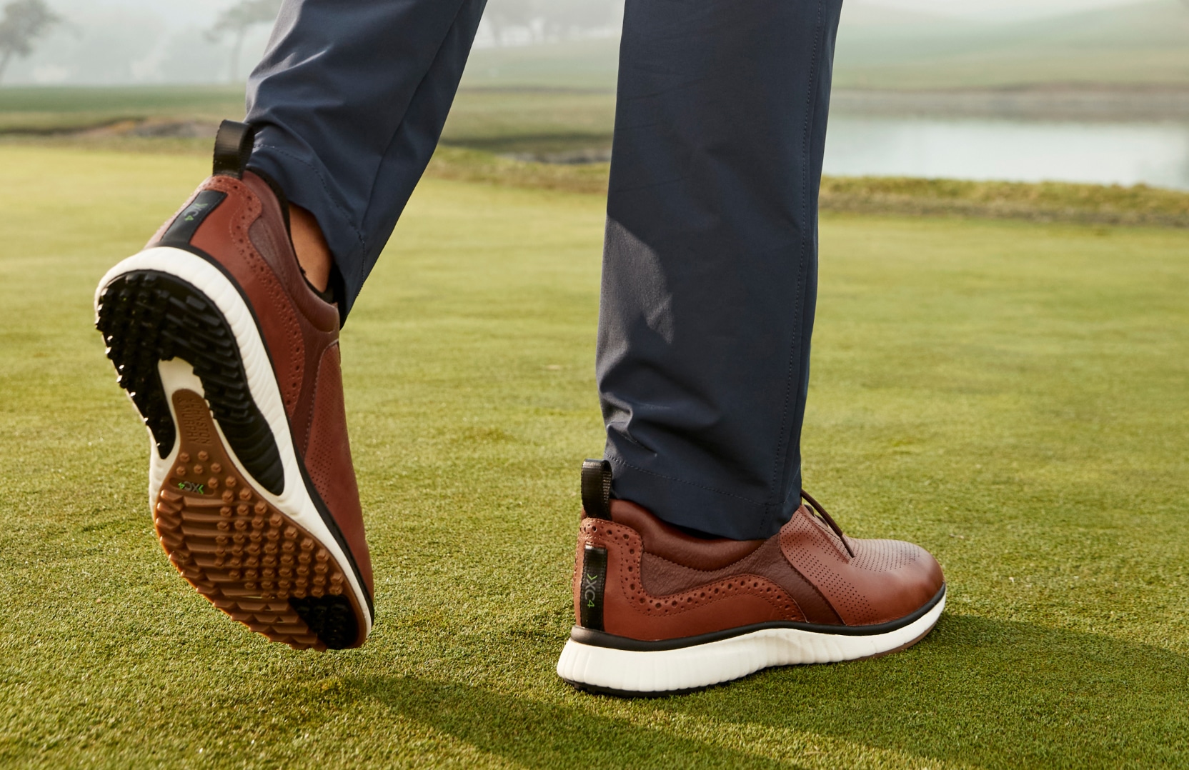 Low-angle view of golf shoes on grass, showing spikeless sole and course background