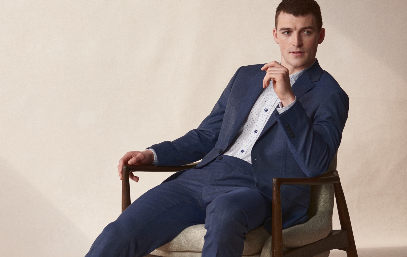 Weekend sale. Premium wool suits 25 percent off. Man seated in a tailored suit.
