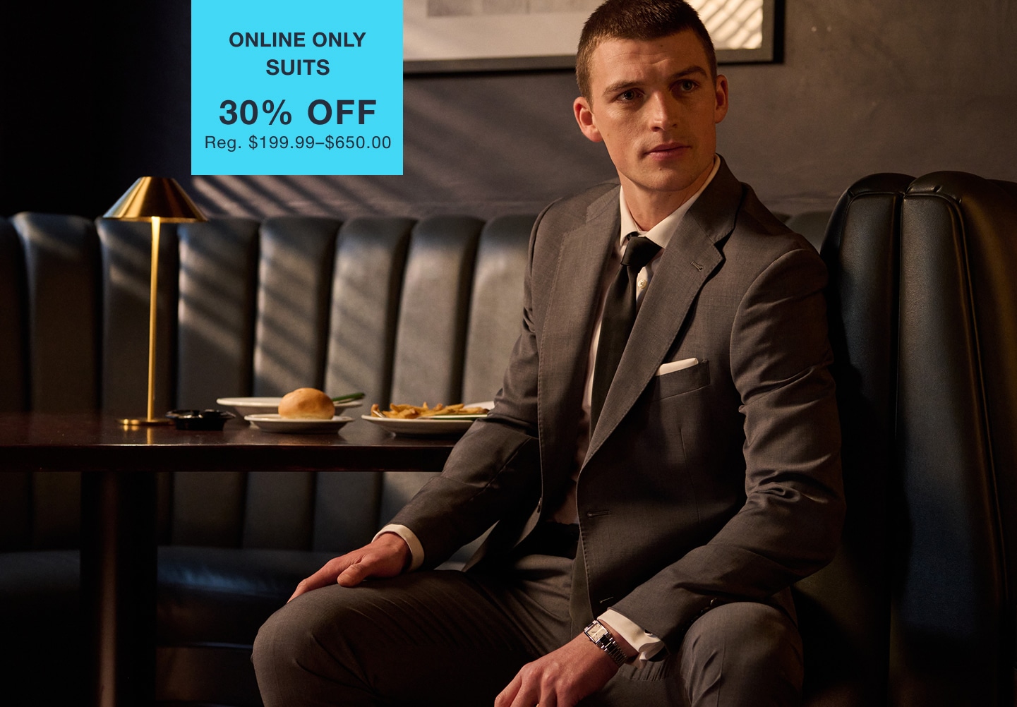 Man wearing a suit in a restaurant. Online only suits 30 percent off. Regular price $199.99 to $650.00.